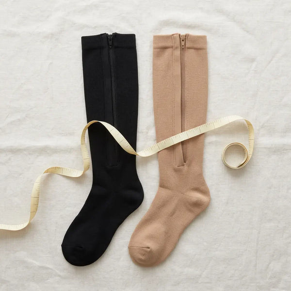 Chaussettes de compression noire et beige à fermeture latérale posées à plat avec un mètre ruban
