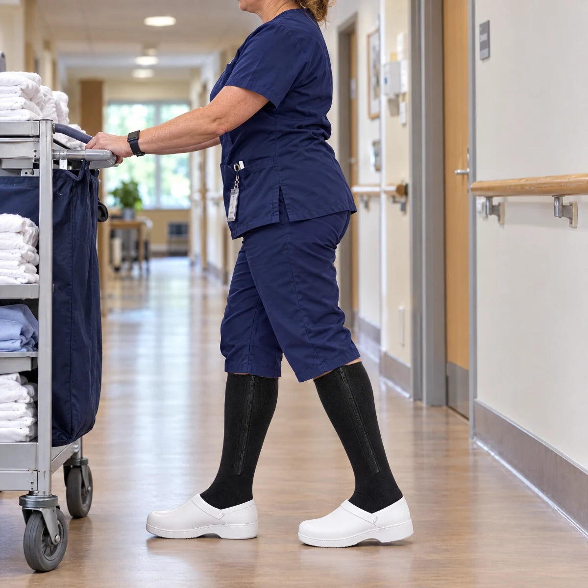 Une soignante marche dans un couloir de service, chaussettes noires sous le pantalon.