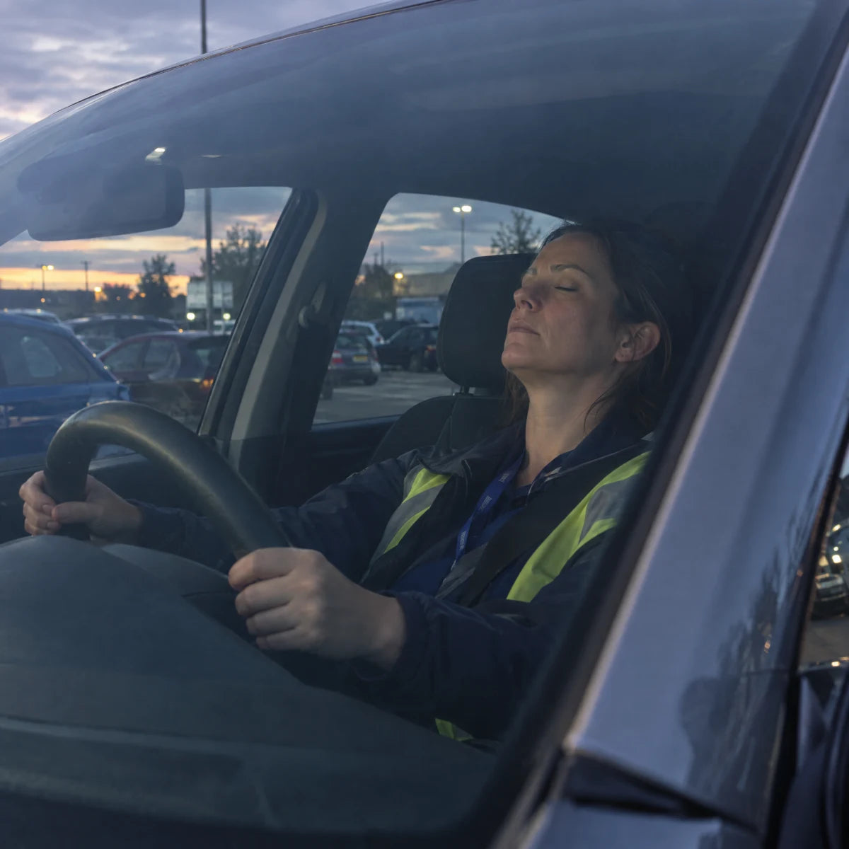 Une femme assise dans sa voiture après son service, épuisée.